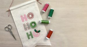 Machine embroidery design featuring stylized lettering spelling out the words, "Ho, Ho, Ho" using a mix of embroidery stitches in a mix of pink, red, bright green, and dark green.