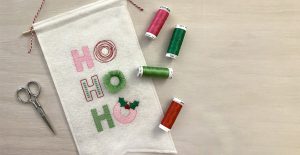 Machine embroidery design featuring stylized lettering spelling out the words, "Ho, Ho, Ho" using a mix of embroidery stitches in a mix of pink, red, bright green, and dark green.