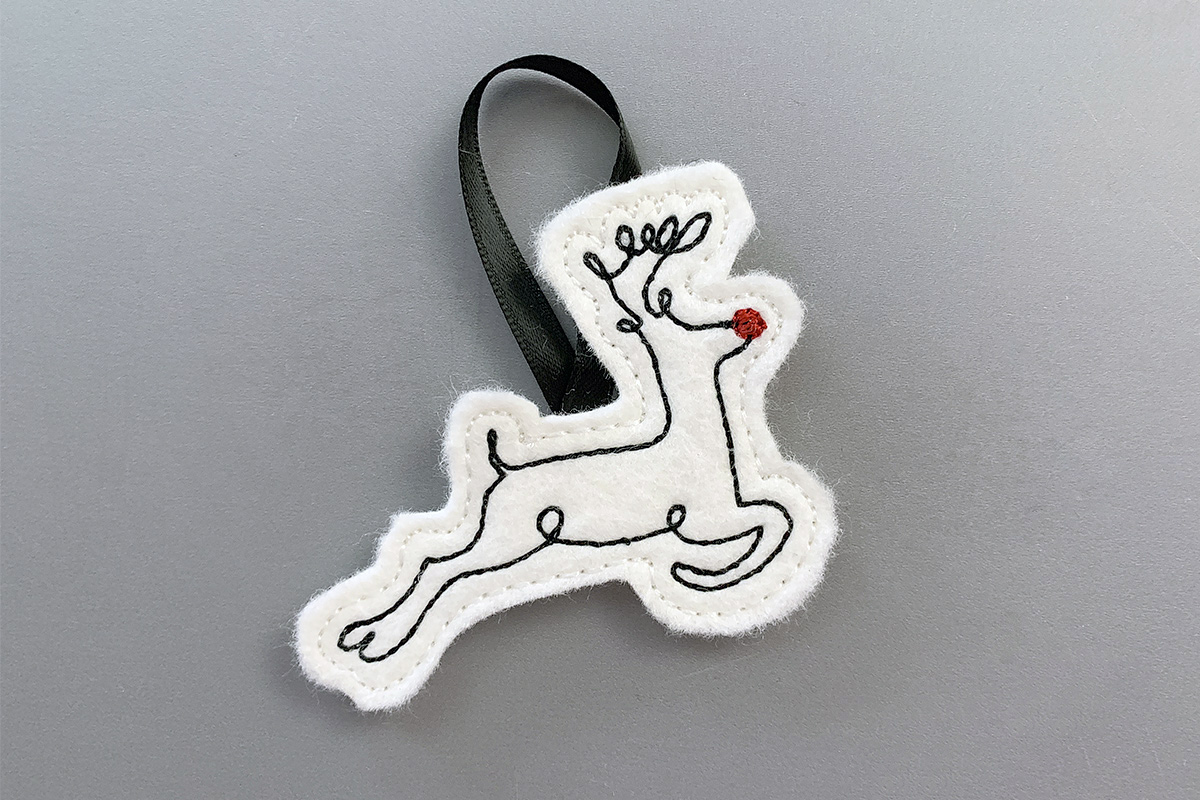 White felt with black embroidered outline of a reindeer featuring a red nose.