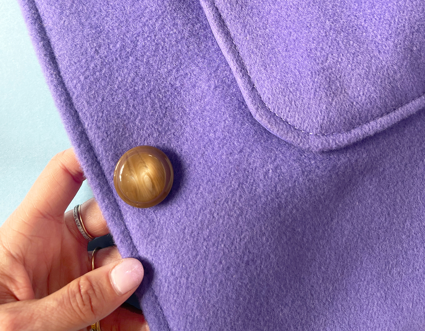 Detail shot of purple wool coating fabric, featuring top stitching and a large brown button.