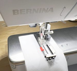 Close up of a BERNINA buttonhole foot sewing a buttonhole in black thread on white fabric.