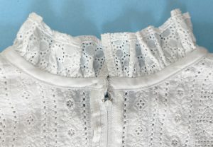Details of the inside of a white eyelet dress. The neckline has a ruffle and is finished with bias tape, the zipper tape is bound with rayon ribbon.
