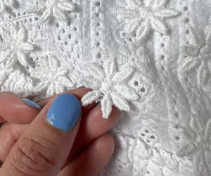 A hand with blue fingernails is touching a small appliqué of a white flower, to show the flower petals are not sewn down.