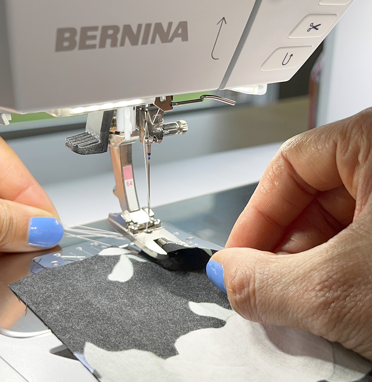 Close up photo of two hands guiding fabric into a BERNINA sewing machine hemmer foot.
