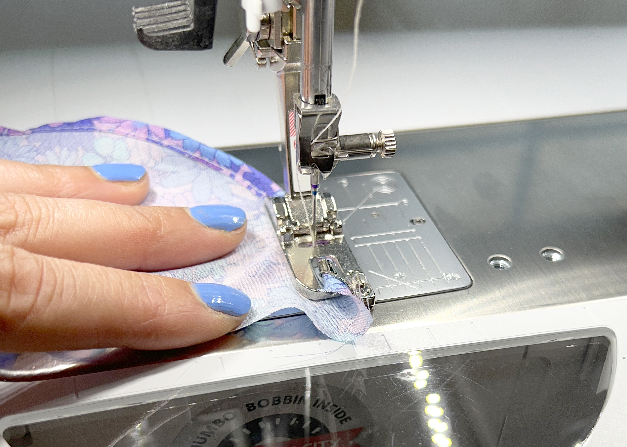 Hemmer foot #63 makes a narrow hem on a curved piece of printed lavender fabric.