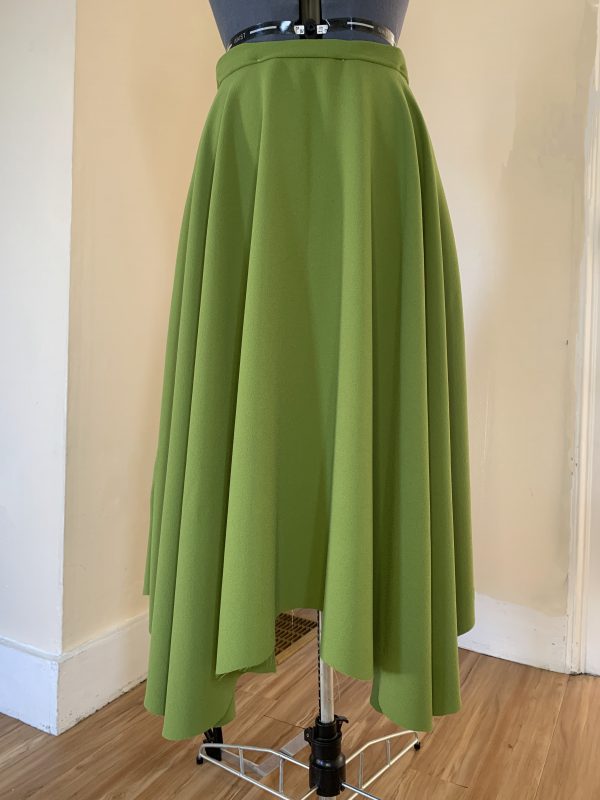 A green skirt on a mannequin with an irregular hem.