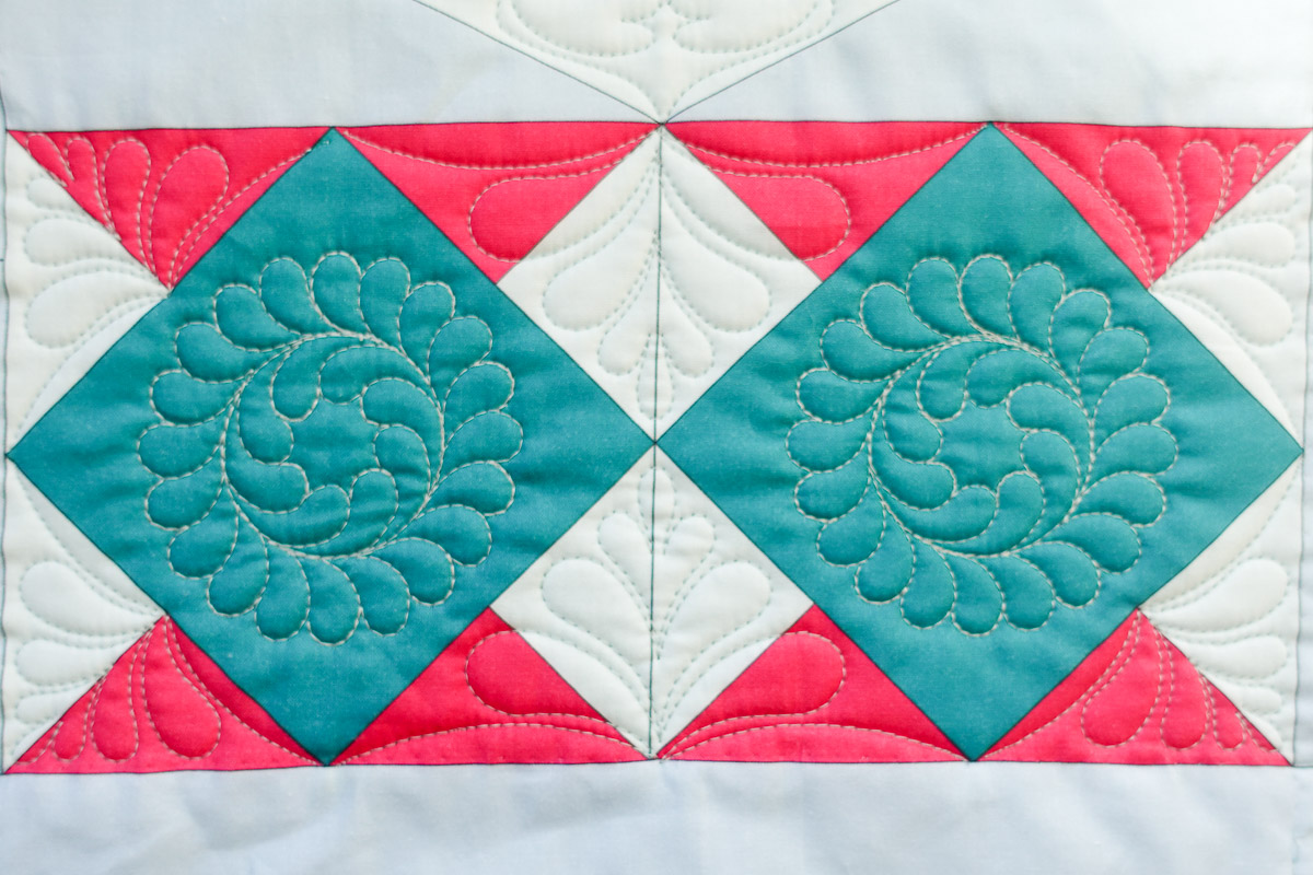 View of the Diamond Block panel on the Jump for Joy Quilt, with quilting over blue, pink, and white diamonds.