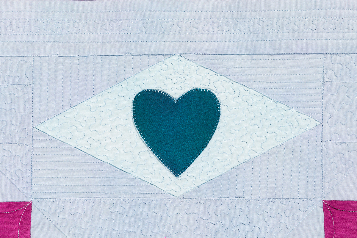 A blue Diamond Heart Applique unit with a white, quilted background.