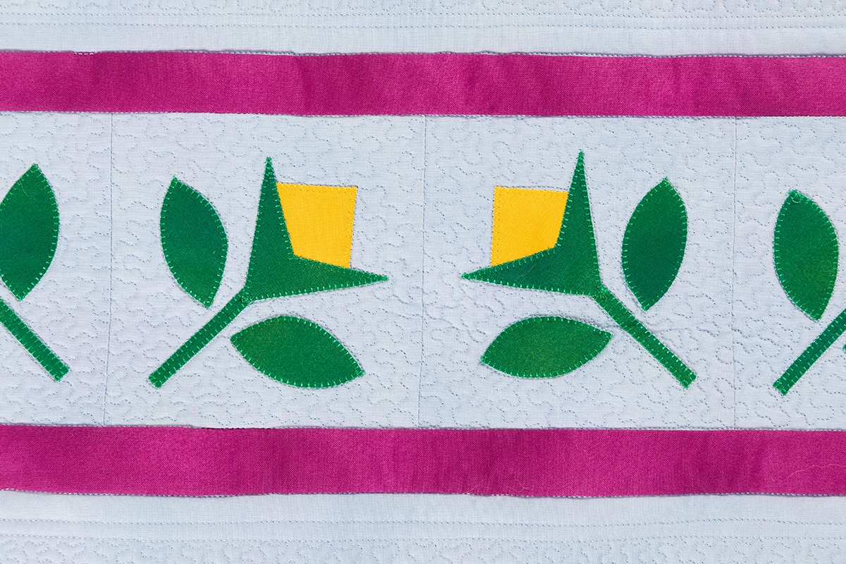 Green and yellow floral applique row with pink borders and a white quilted background.