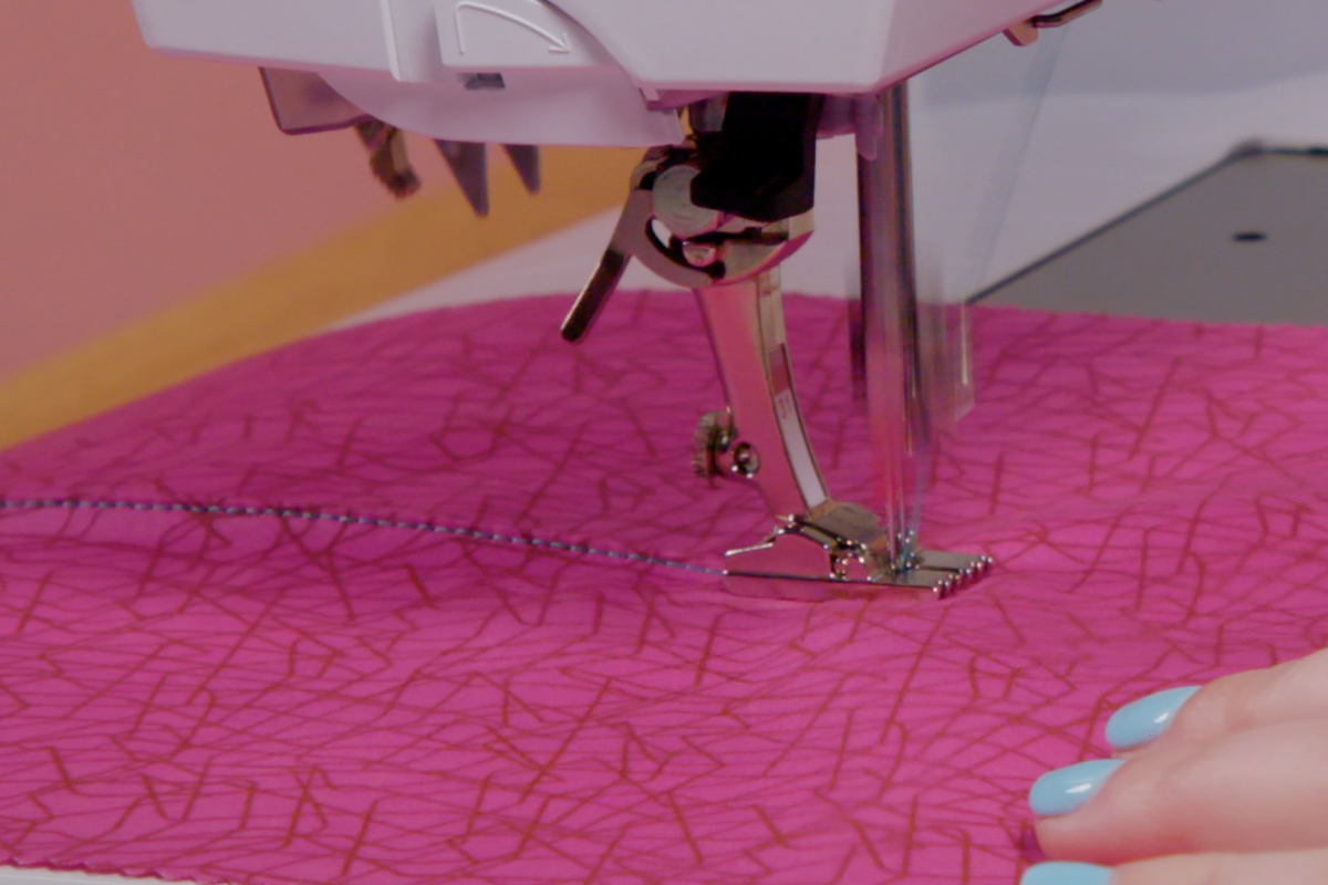 side view of pink fabric being fed through the sewing machine to create pintucks
