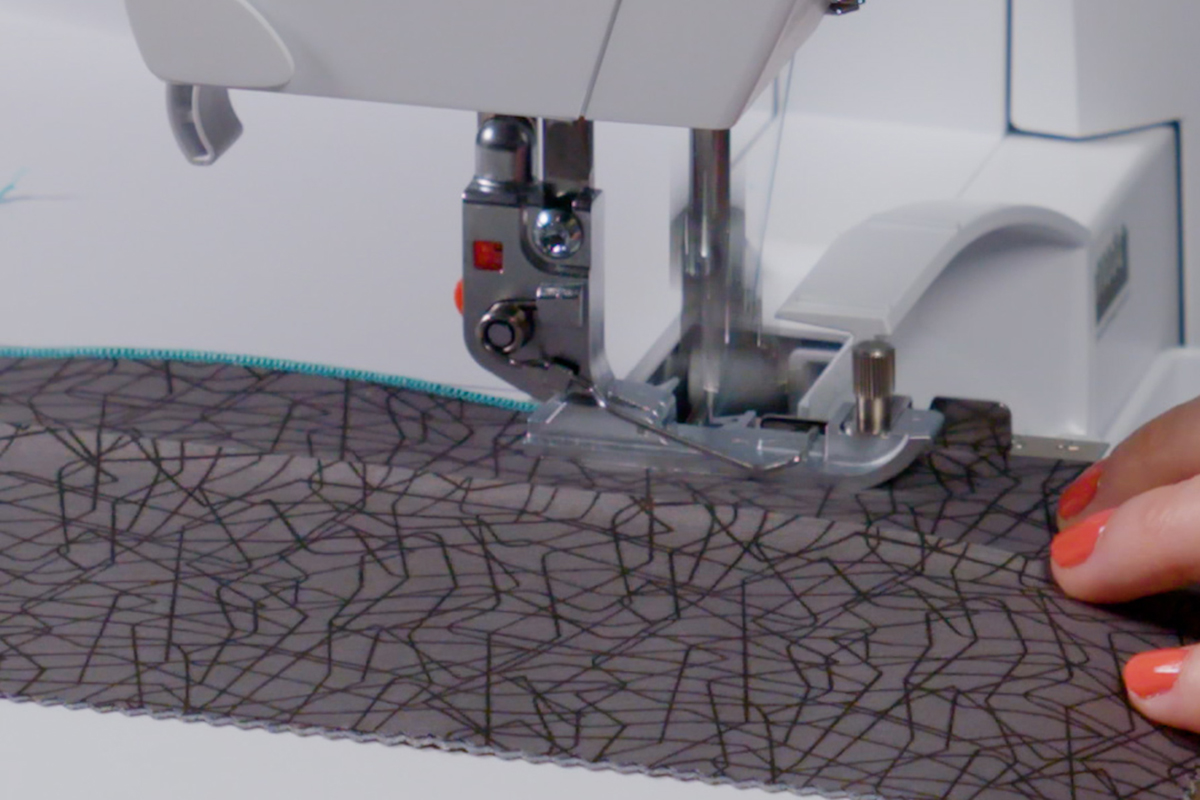 side view of black fabric being fed through a serger to create pintucks