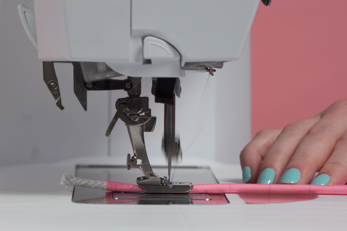 white cord wrapped in pink fabric, being fed through a sewing machine