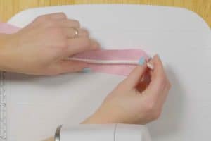 overhead view of hands wrapping pink fabric around a white cord