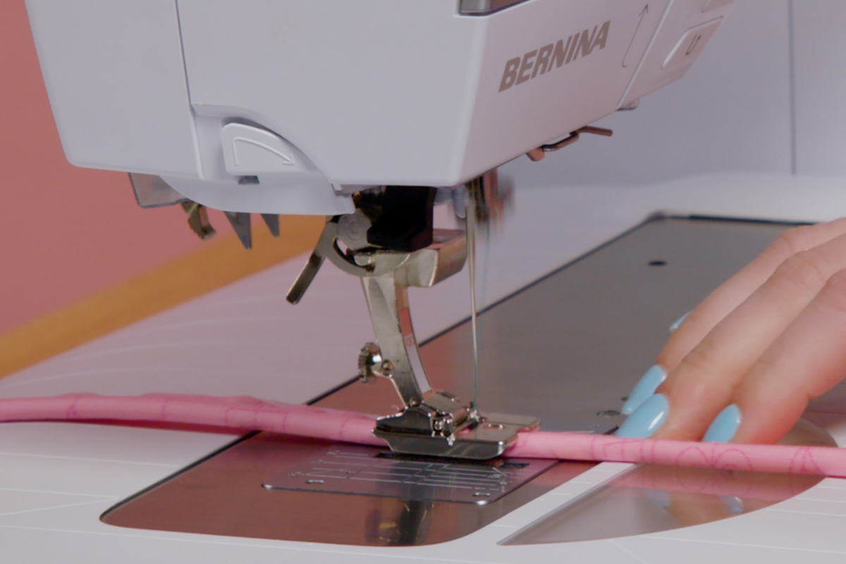side view of pink-fabric wrapped cord being fed through the sewing machine