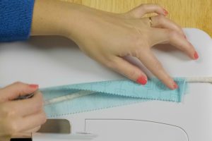 Serger wrapped cording; overhead view of blue fabric being wrapped around white cording