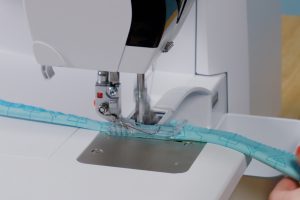 Serger piping; side view of blue-fabric wrapped cording being fed through a serger