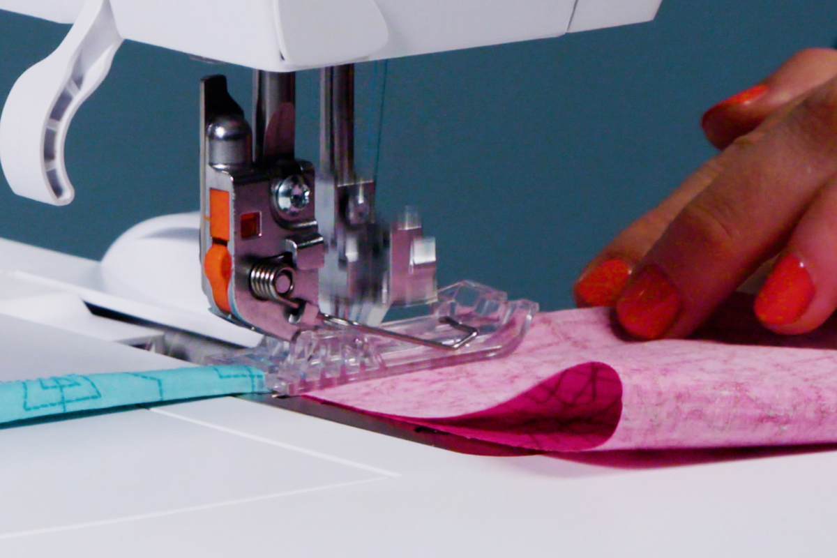 pink and blue fabric, with cording, being fed through a serger