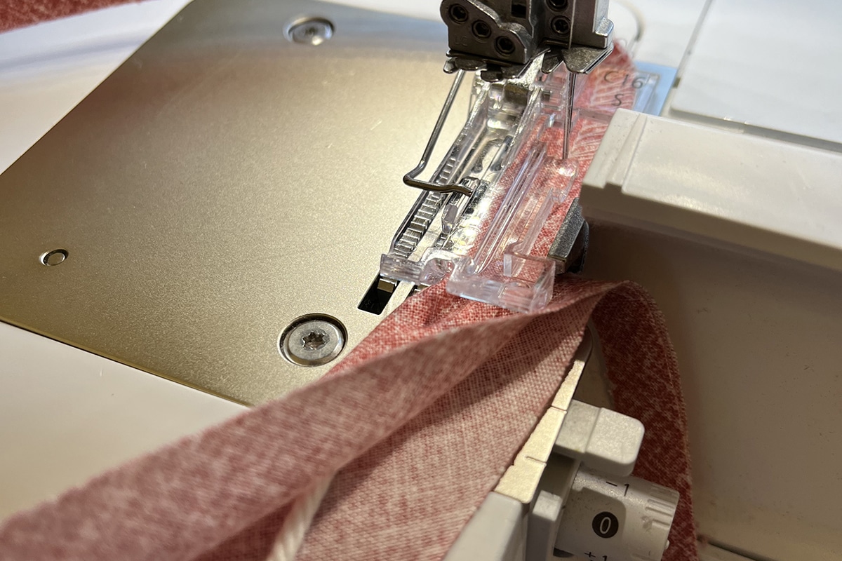 white cord, wrapped in pink fabric being fed through a serger