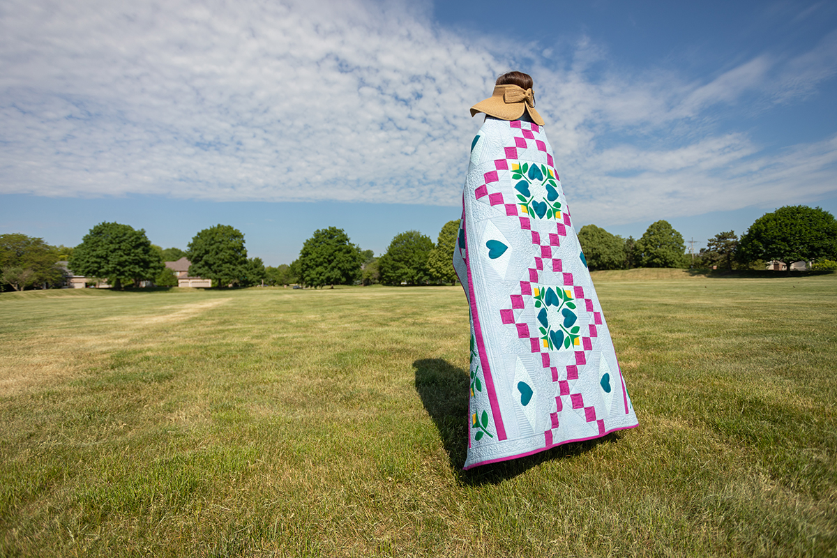 Jump for Joy quilt draped around a woman walking in a sunny field.