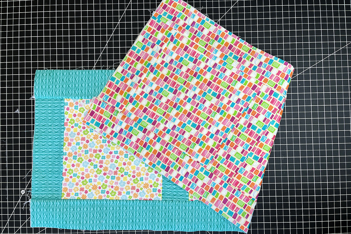 overhead view of teal borders sewn onto squares of multi-colored fabric.