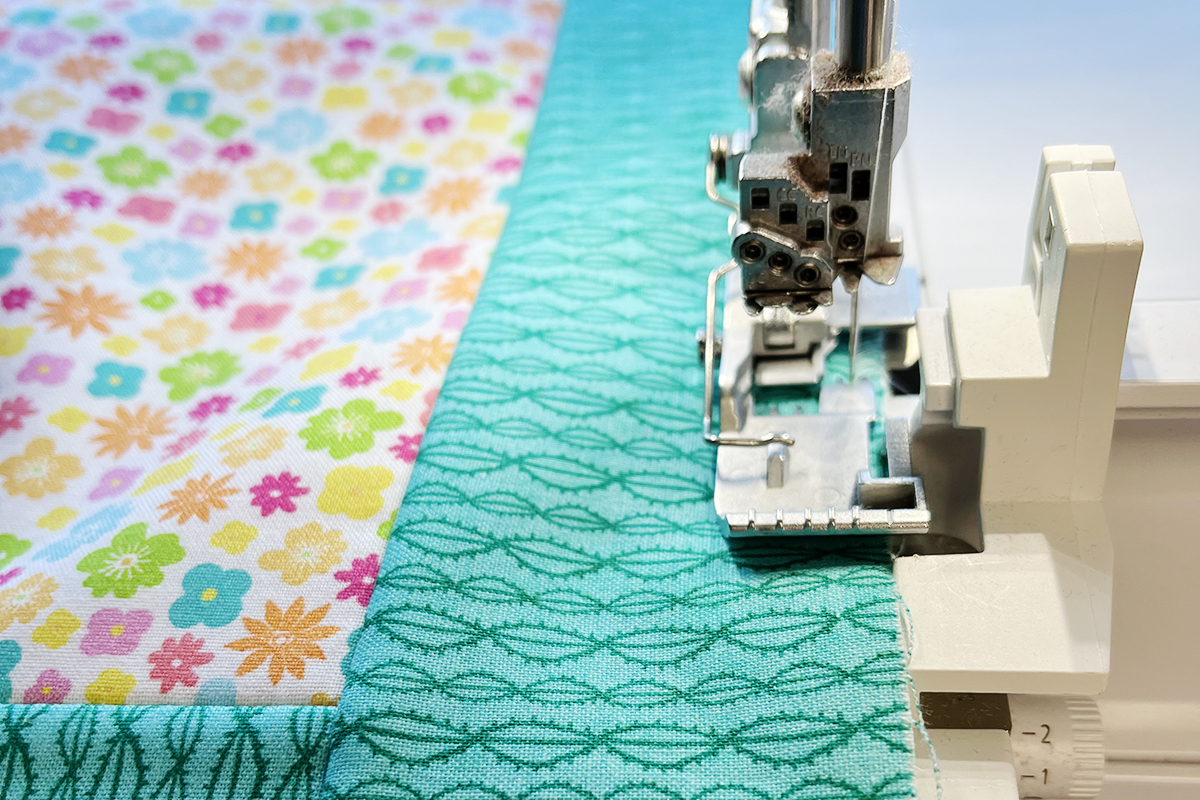 front facing view of teal fabric being fed through a serger.