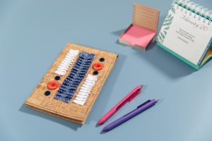 Cork notebook cover on a blue counter with office supplies arranged around it