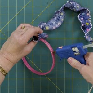gluing the beaded, gathered fabric to a pink headband using a hot glue gun