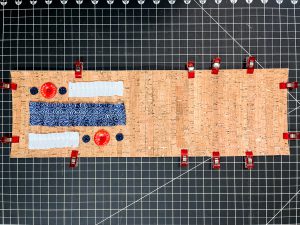 An overhead view of ribbon and buttons arranged on the cork notebook cover