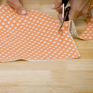 : side view of a left-handed sewer using sheers to cut a circle out of orange fabric