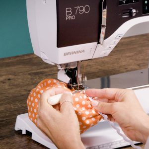 sewing rickrack to an orange fabric bowl, using a stiletto to keep things aligned