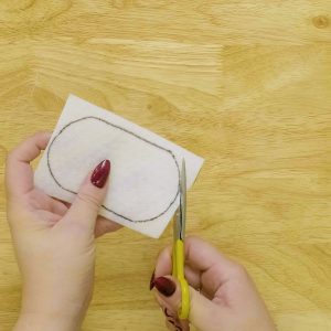 Using scissors to cut out applique shape from fusible woven