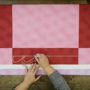 Overhead view of red and pink checkered quilt with ruler guide aligned with stitches