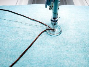 Close-up view of brown cording being couched onto blue fabric