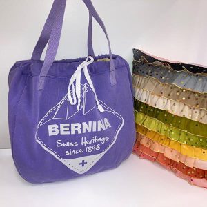 Purple BERNINA toe bag next to rainbow ruffled pillow on white background