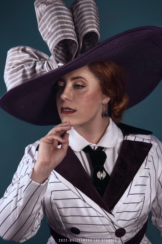 Woman wearing purple-based straw hat with black and white-striped top and jacket