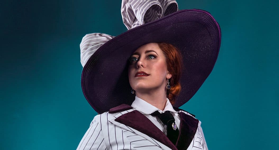 Woman wearing purple-based straw hat with black and white-striped top and jacket