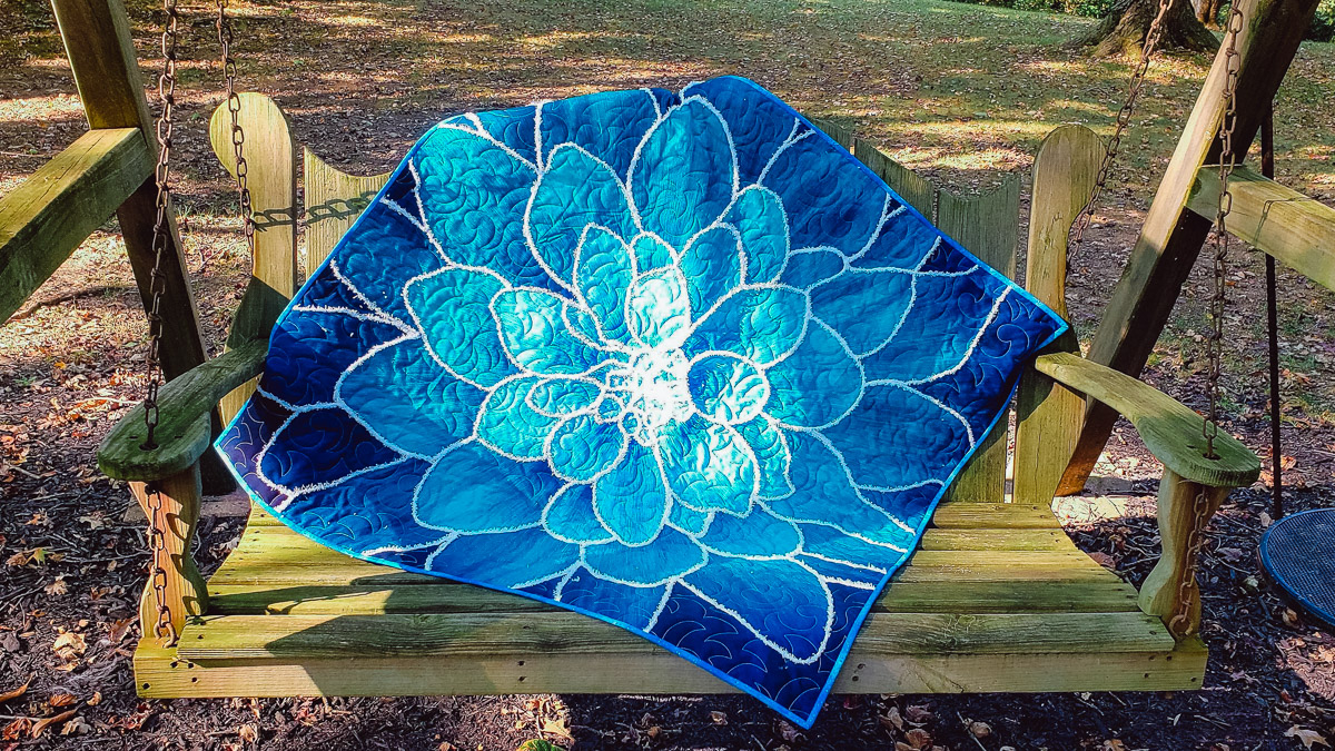 finished quilted and couched blue floral quil displayed on a wooden swing