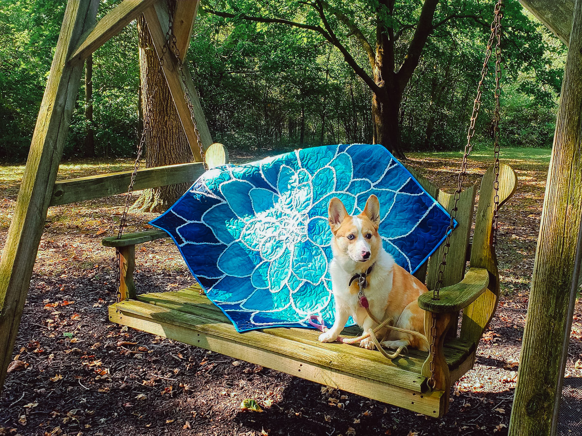 finished quilted and couched blue floral quil displayed on a wooden swing next to a puppy