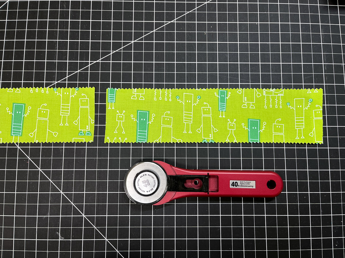 Green fabric strip and rotary knife on a black cutting board