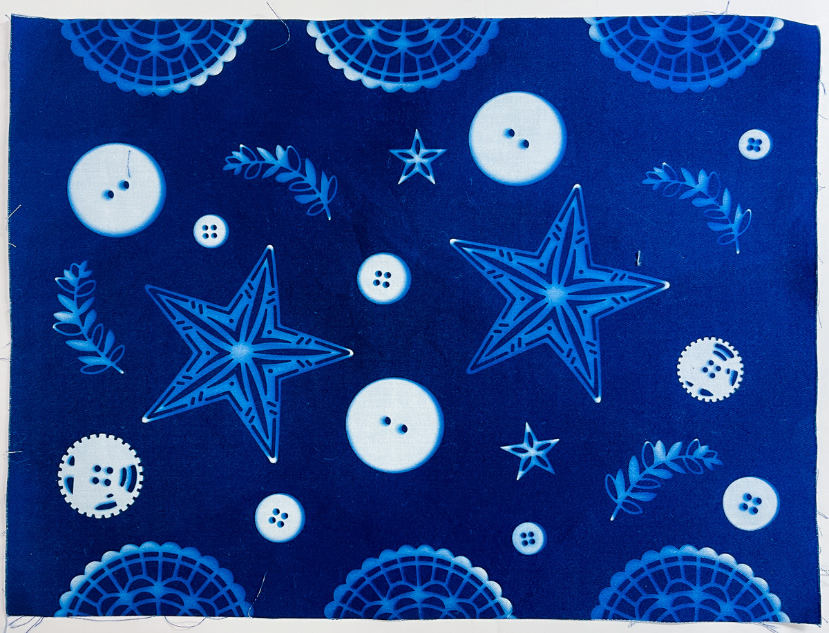 Buttons and card-making supplies final result showcasing white imprints on a brilliant blue fabric