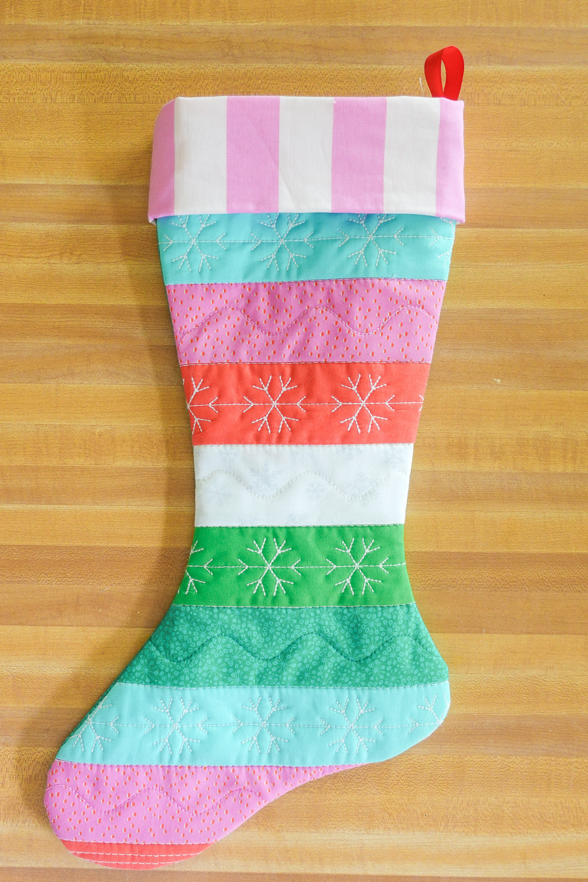 Blue, red, pink, and green quilted stocking on wood table