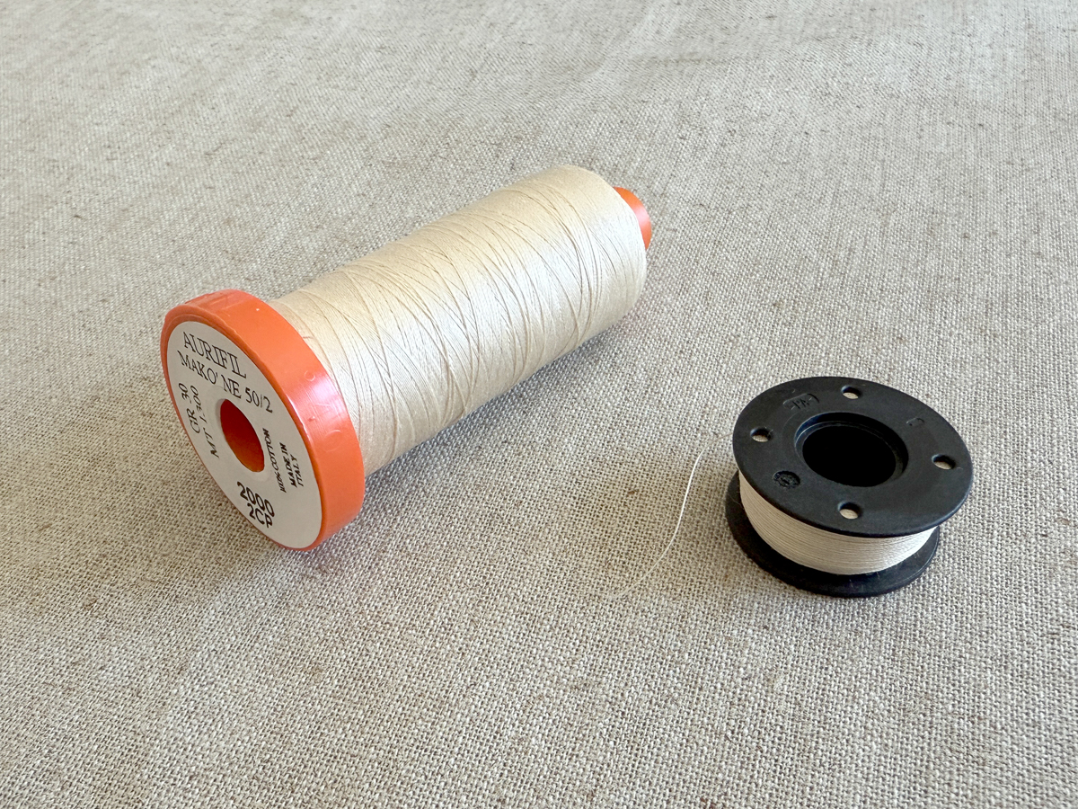 Thread and bobbin arranged on cream linen fabric