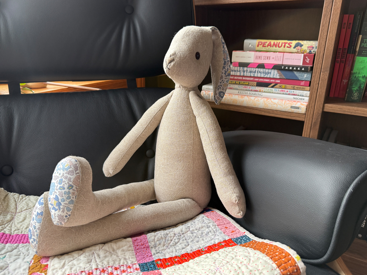 Flora Lapin Rabbit sitting propped up on a chair and quilt