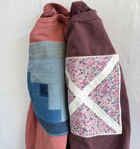 two sweatshirts with quilt blocks quilted on to them hanging on a wall