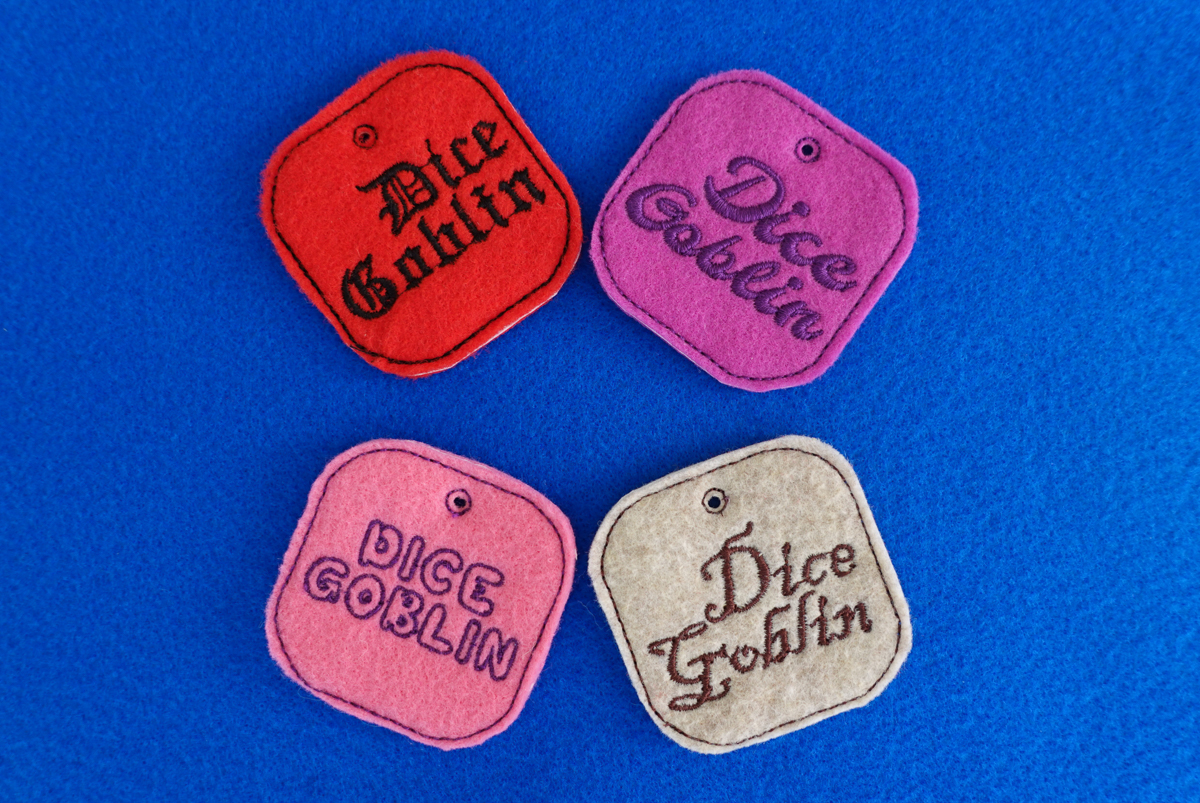 Pink, purple, cream, and red felt tags that say dice goblin