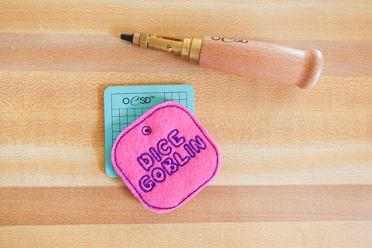 Dice Gobling bag tag arranged on wood background with hole punching tools