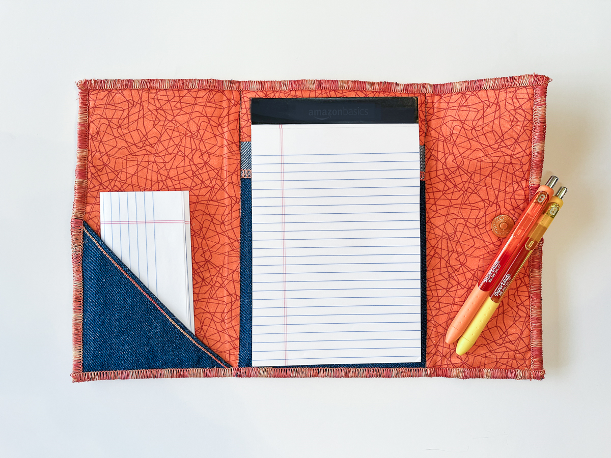 Open notebook folio with orange lining, pens, and white notepad