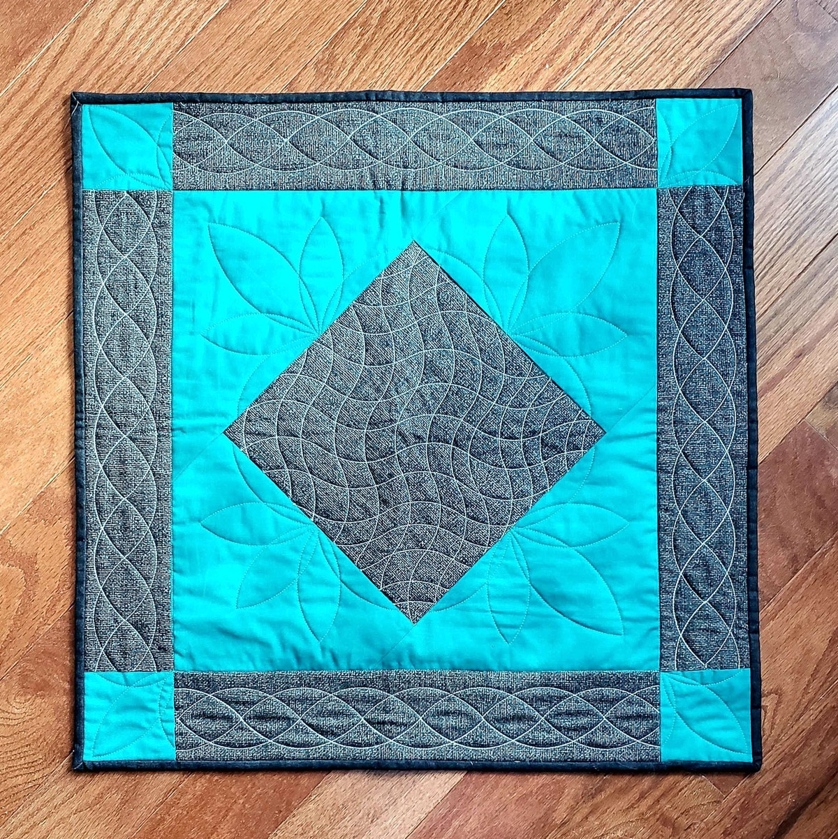 Overhead view of the Curvy Quilting Table Topper, with teal and gray fabric on a wood floor