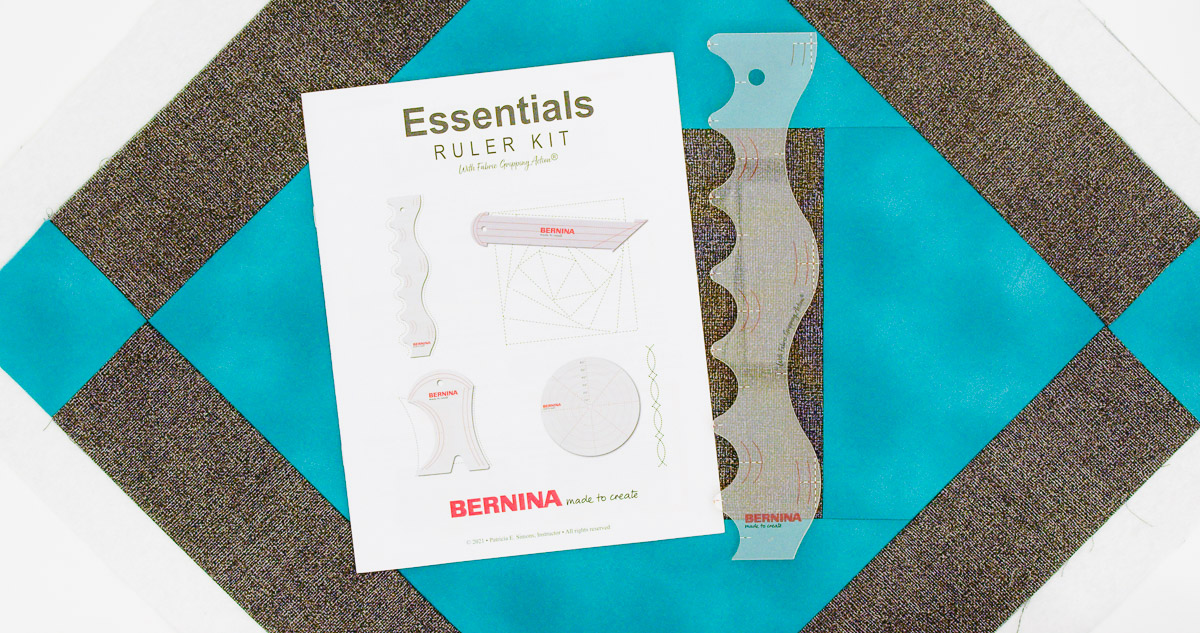 Overhead view of teal and gray fabric with the manual and Squiggle Ruler from the BERNINA Essentials Ruler Kit