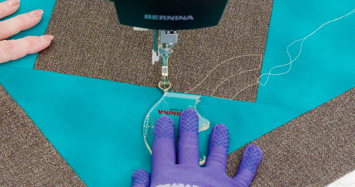 Close-up photo of purple-gloved hands quilting curvy lines on teal and gray fabric with a BERNINA Ruler.